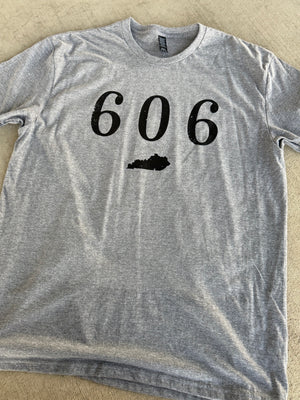 A heather gray crewneck t-shirt laid flat on a beige textured surface, featuring the black printed numbers '606' and a Kentucky state silhouette graphic on the chest.
