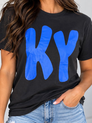 A woman wearing a black short-sleeve t-shirt with a large blue 'KY' graphic on the front, paired with light blue jeans.