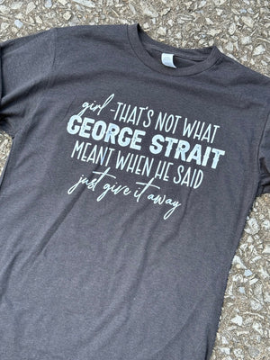 Front of dark heather gray short sleeve t-shirt with the text "girl - That's not what George Strait meant when he said just give it away." printed in white.  The shirt is laying on the floor.