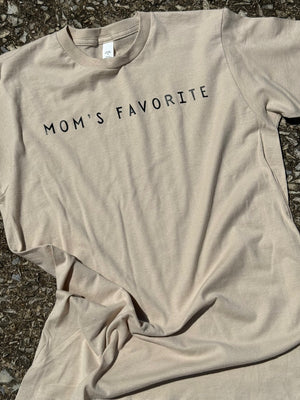 Front of beige short sleeve T-shirt with the  text "Mom's favorite" printed in black on it. The shirt is laying flat on the floor.
