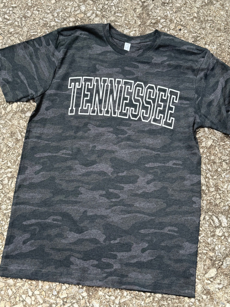 Black camouflage short sleeve t-shirt with 'TENNESSEE' text in an outline font printed in white. Shirt is laying on the floor.