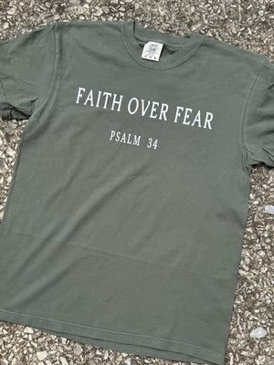 Green t-shirt with 'Faith Over Fear Psalm 34' printed in white on the shirt. Shirt is laying on the floor.