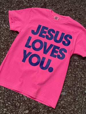 Hot Pink short sleeve t-shirt with Large 'Jesus Loves You' text printed in navy blue. Shirt is laying on floor.