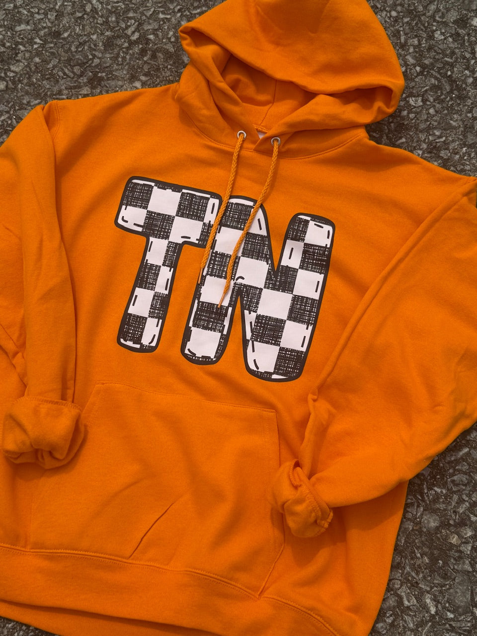 Bright Orange long sleeve hoodie with large black and white checkorboard TN graphic. Hoodie is laying on the floor