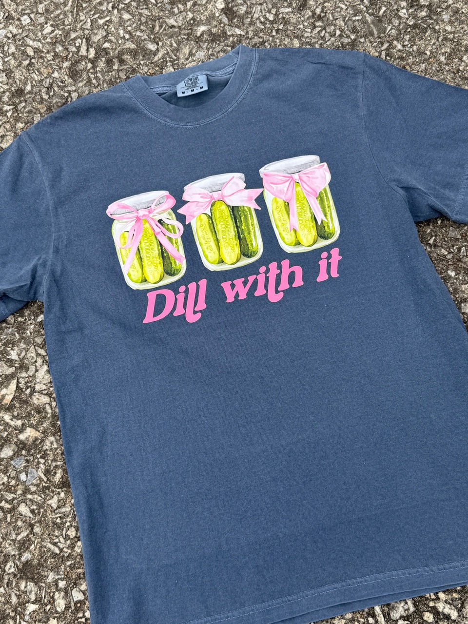 Front of Blue short sleeve T-shirt with three pickle jars with pink bows and the text "Dill with it" printed in pink under the pickle jars. The shirt is laying on the floor.