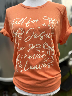 Orange t-shirt with Fall for Jesus he never leaves with bows and stars in a cream text on a mannequin against a blurred background
