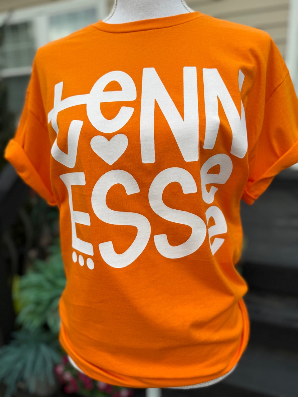 Orange t-shirt with big white text that says Tennesee with a heart on a mannequin against a blurred background