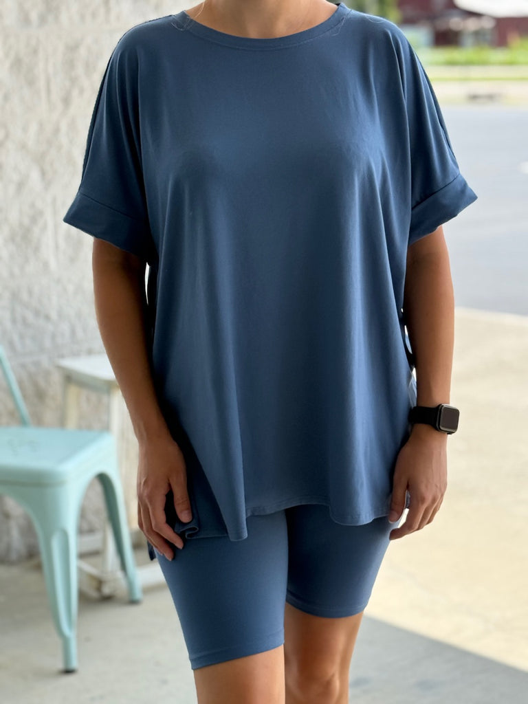 Woman wearing a dusty blue short sleeve shirt and dusty blue biker shorts.