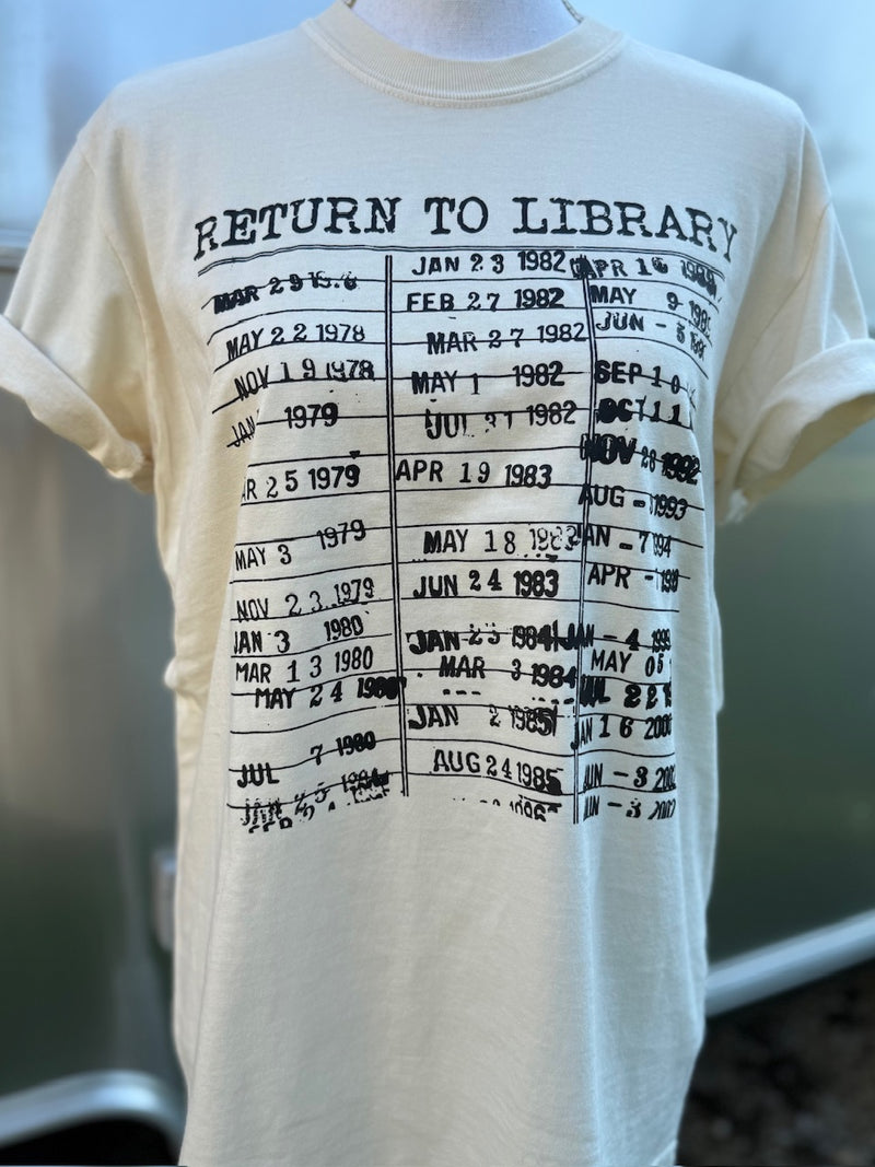 Cream t-shirt with printed library due date system in black. A mannequin is wearing this shirt standing in front of a blurry background.