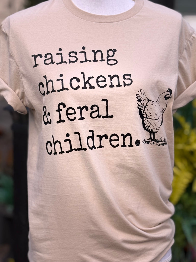 Front of short sleeve pink t-shirt with the text "Raising chickens & feral children." with a vintage outline of a chicken printed in black on the shirt. The shirt is on a mannequin standing in front of a blurry background.